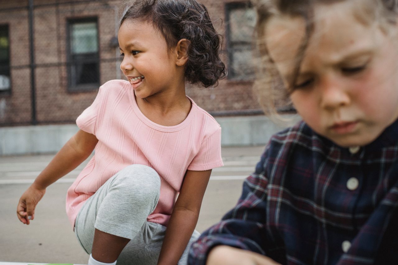 Two young girls smiling and playing outside on a sunny day.