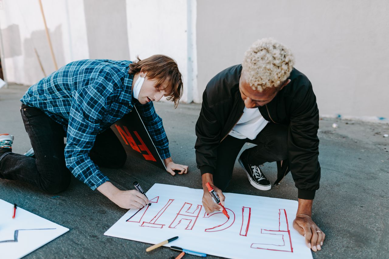 Two young activists design protest signs on the pavement, expressing empowerment.